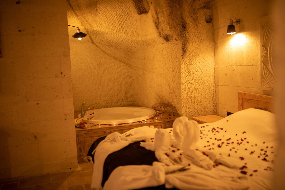 A dimly lit room with a bed, a small table with a glass, and a wall-mounted light fixture.