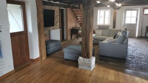 Een ruime woonkamer met houten vloeren, een stenen zuil en een open haard van baksteen.
