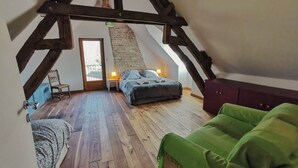 Een slaapkamer in zolderstijl met een schuine kap, houten balken, een bed, een stoel en een kleine tafel met een lamp.