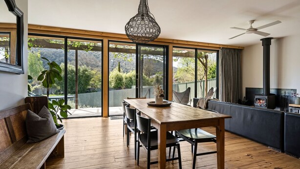 A spacious room with a wooden dining table, a bench, and a large window offering a view of a garden and hills. - One Bright Stay in beautiful Bright (Bright)
