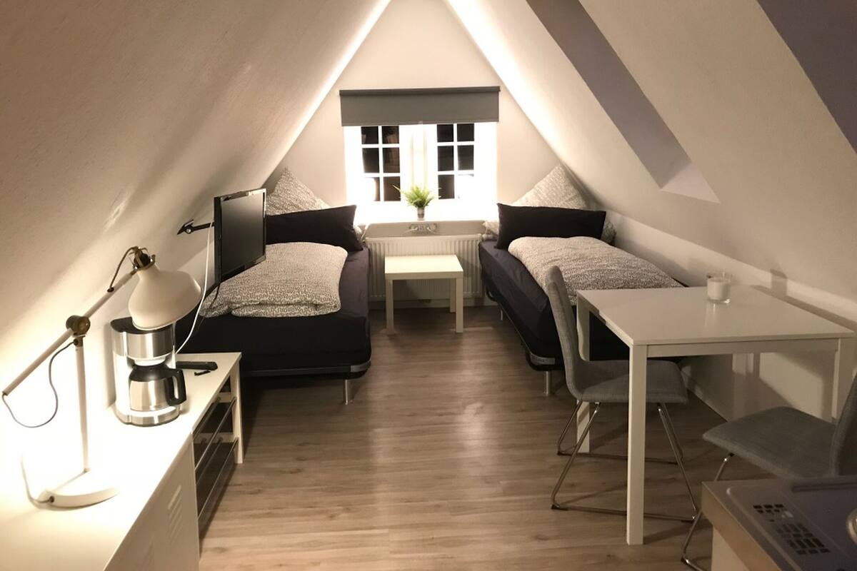 Ein gemütliches Schlafzimmer im Dachgeschoss mit zwei Betten, einem Schreibtisch, einem Stuhl und einem kleinen Tisch.