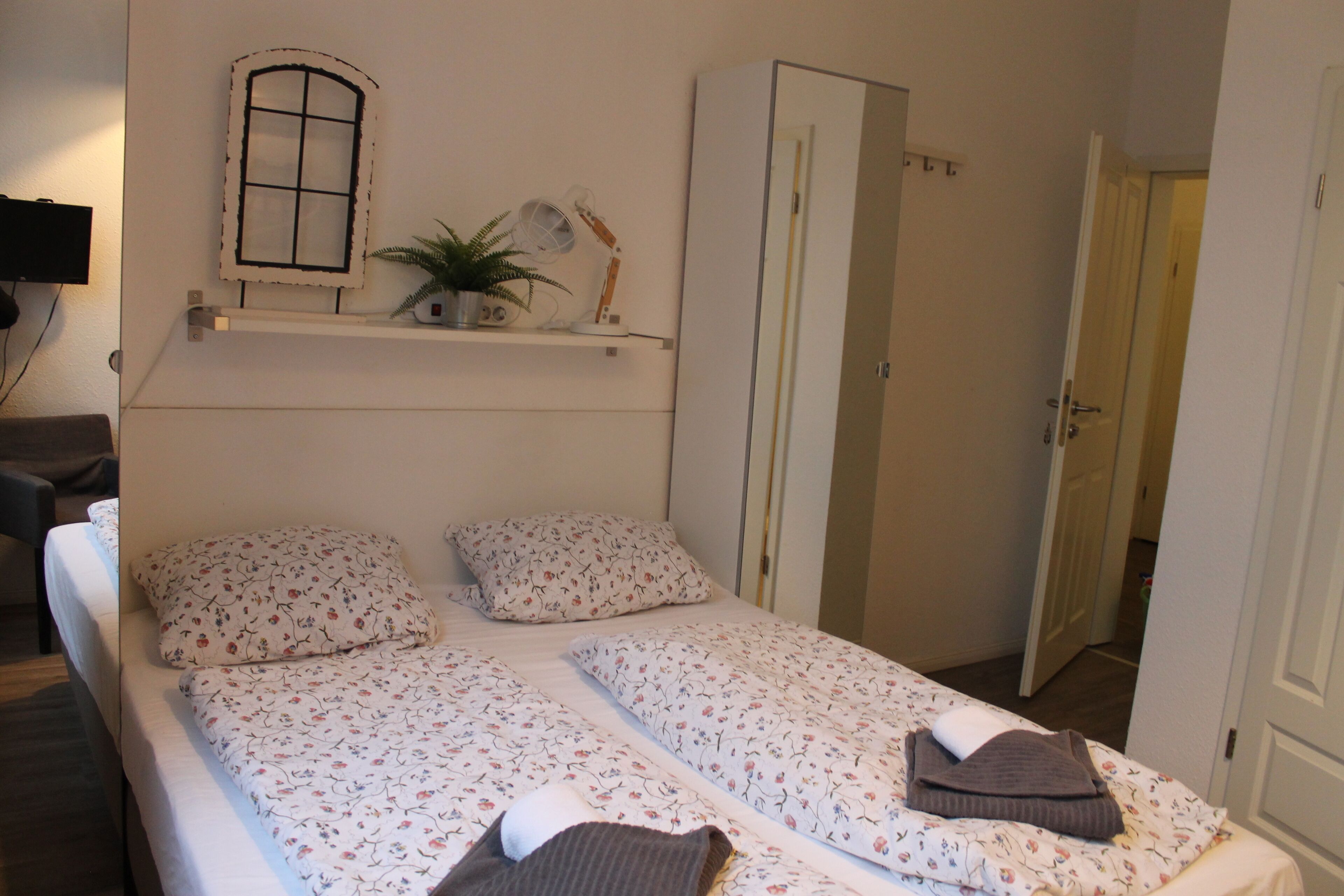 A bedroom with two single beds, a wardrobe, a shelf with decorative items, and a small window.