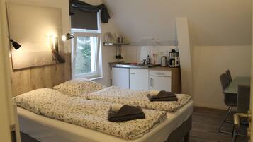 A bedroom with two beds, a small kitchenette, and a dining area.