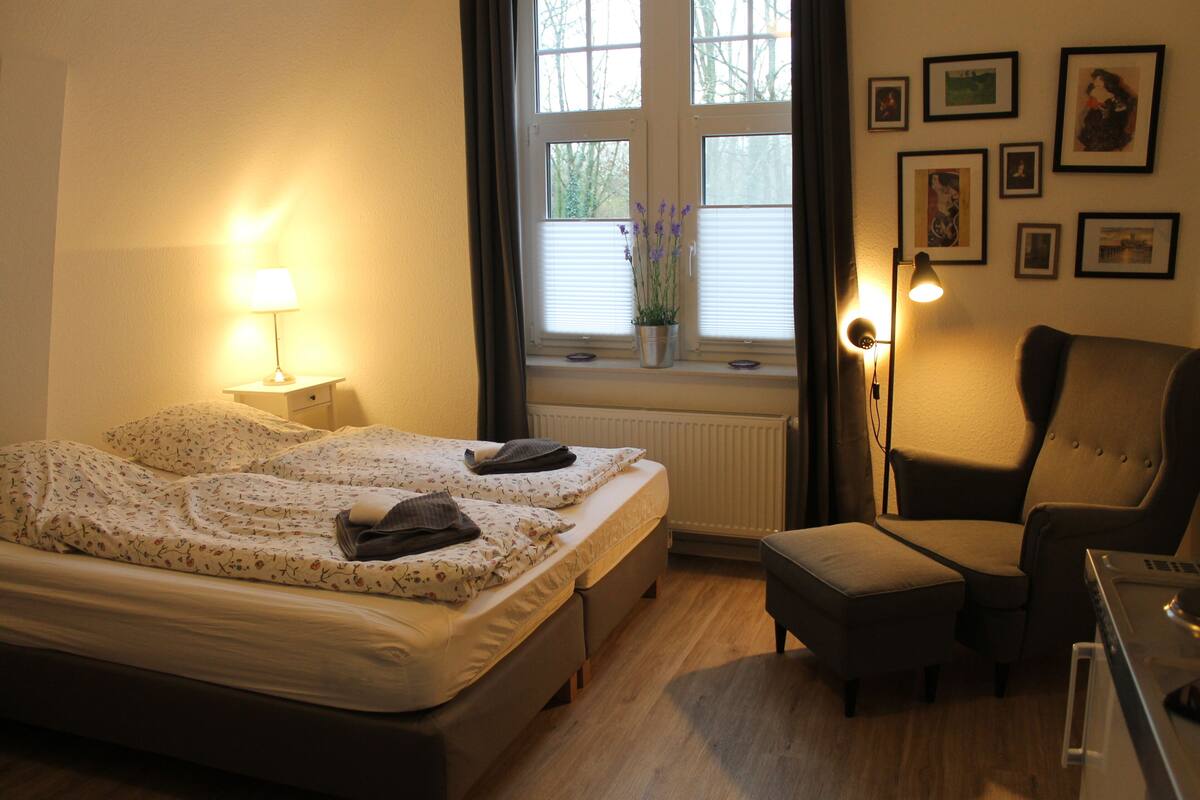 Ein Schlafzimmer mit Bett, Nachttischlampe, Stuhl und einem Fenster mit Jalousien.