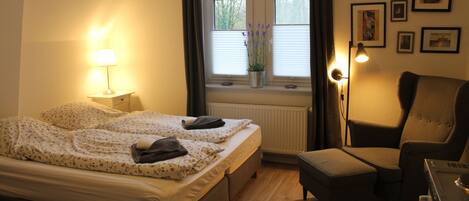 A bedroom with a bed, bedside lamp, chair, and a window with blinds.