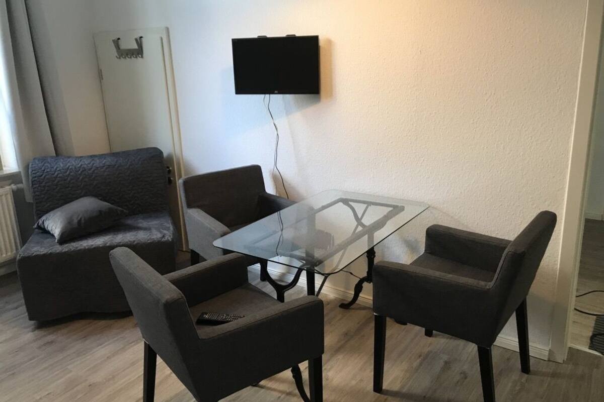 Ein modernes Wohnzimmer mit einem Glastisch, zwei Sesseln, einer Couch und einem flachbildfernseher an der Wand.