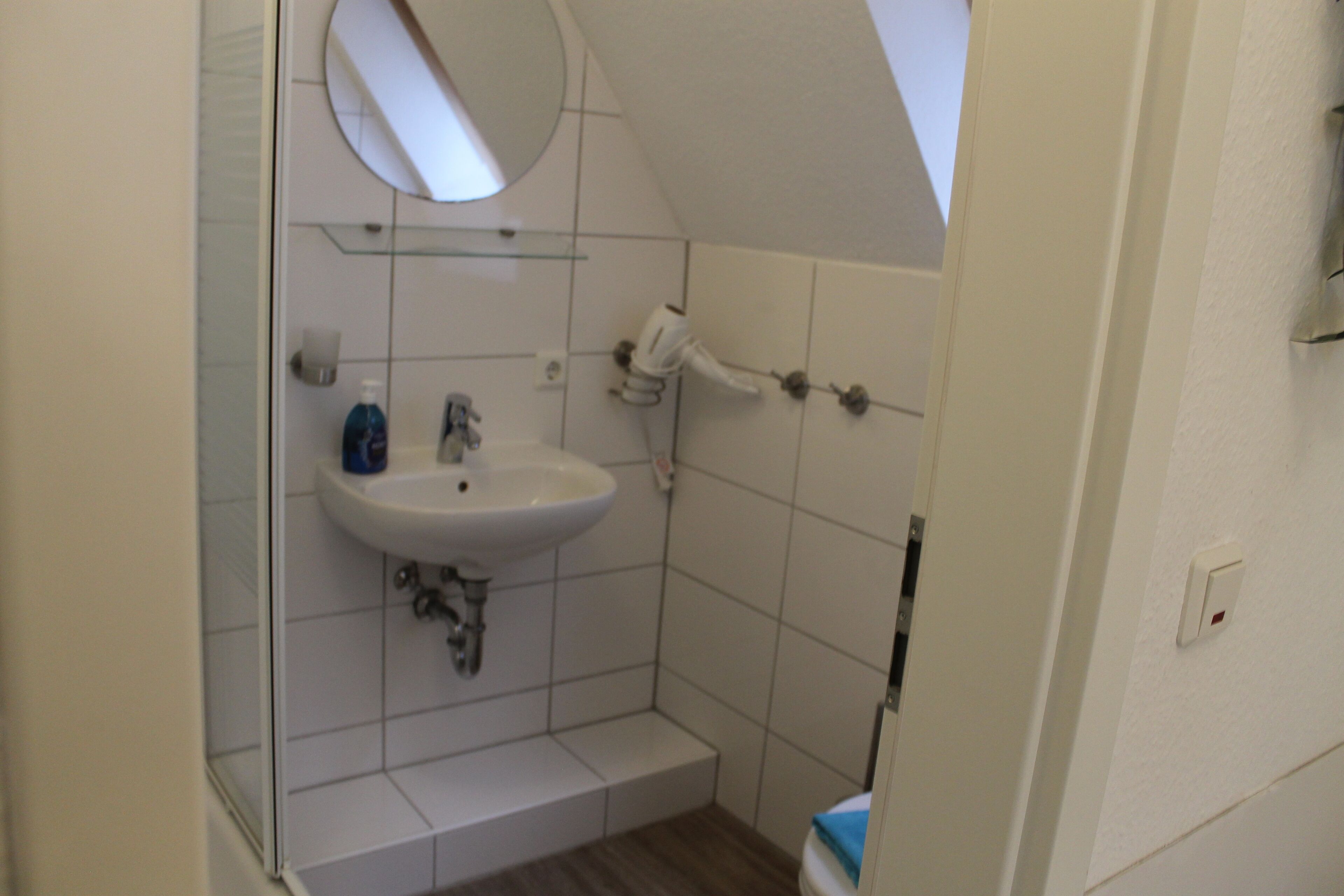A small bathroom with a white sink, a mirror, and a shower.