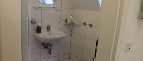 A small bathroom with a white sink, a mirror, and a shower.