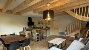 A spacious living area with a wooden ceiling, a dining table with chairs, a sofa, and a staircase. - Triplex - RDC les Ecrins (Le Lioran)