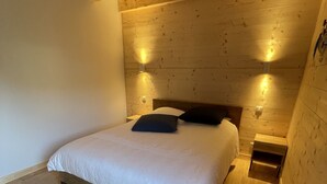 A bedroom with a wooden ceiling, a bed with white bedding, and two wall-mounted lights. - Triplex - RDC les Ecrins (Le Lioran)