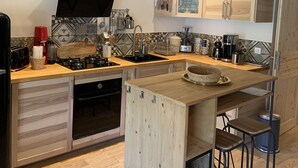 A modern kitchen with wooden cabinets, a central island, and a built-in oven. - Triplex - RDC les Ecrins (Le Lioran)