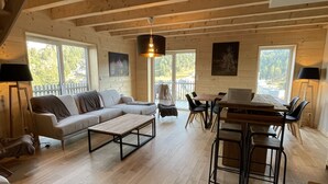 A spacious living room with a sofa, coffee table, and dining area with chairs. There is a staircase leading to an upper level. - Triplex - RDC les Ecrins (Le Lioran)