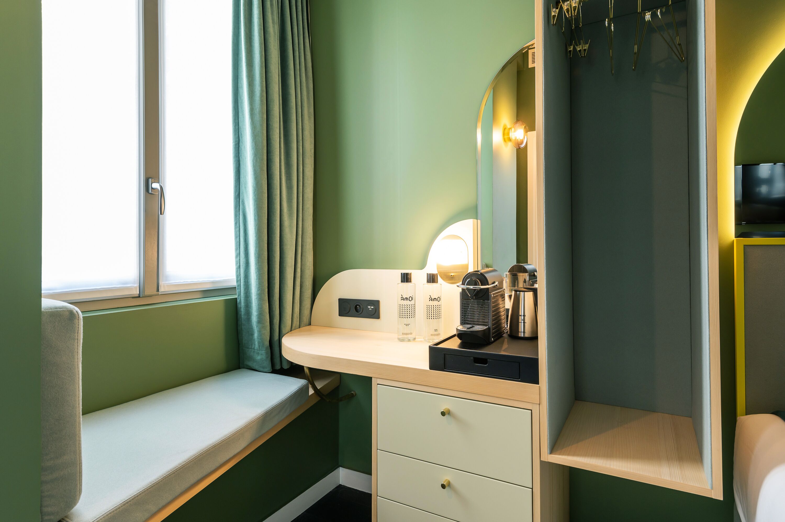 A compact room with a window, a bench, a vanity with a mirror, and a small table with toiletries.