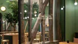 A modern interior with a glass partition, wooden beams, and round tables with stools. - Hôtel Amoi Paris (Paris)