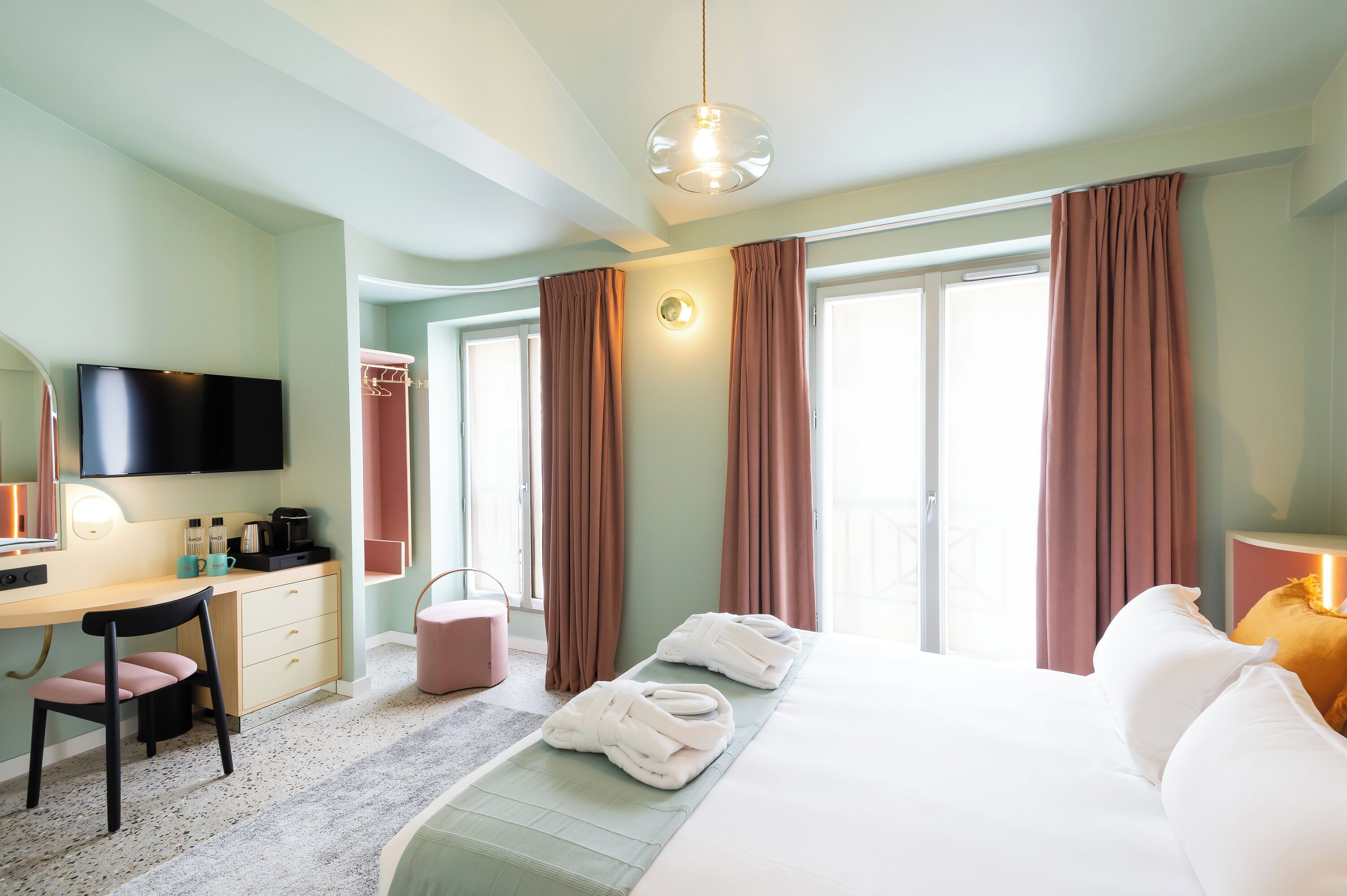 A hotel room with a bed, a desk with a chair, a television, and a window with curtains.