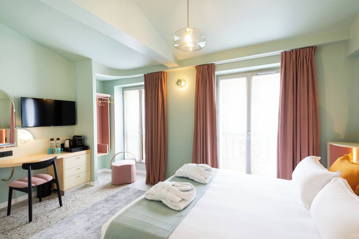 A hotel room with a bed, a desk with a chair, a television, and a window with curtains.