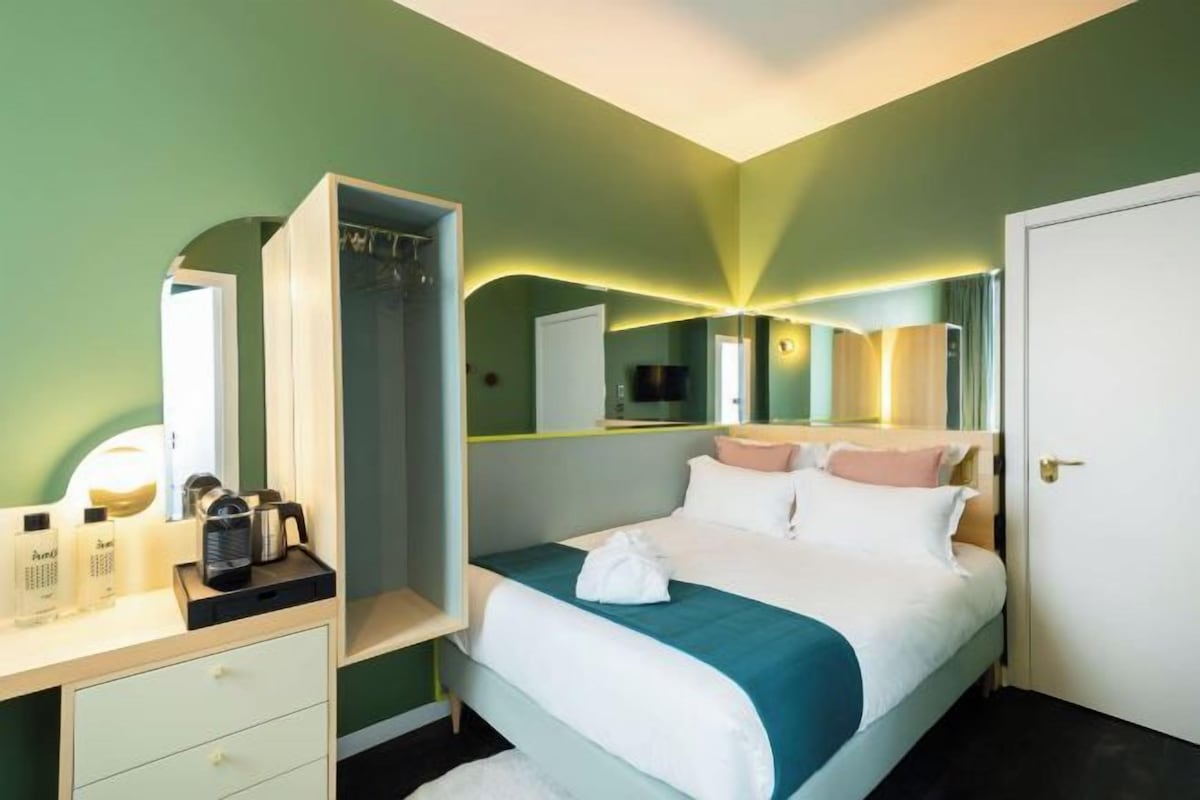 Una habitación de hotel con cama, armario, espejo y mesita de noche con artículos de aseo.