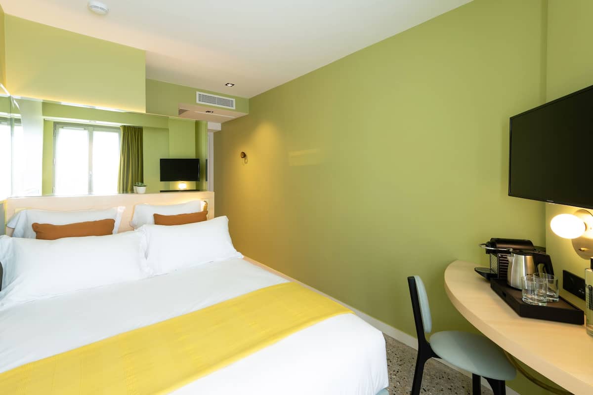 A hotel room with a bed, a desk with a chair, a flat-screen TV, and a window with curtains.