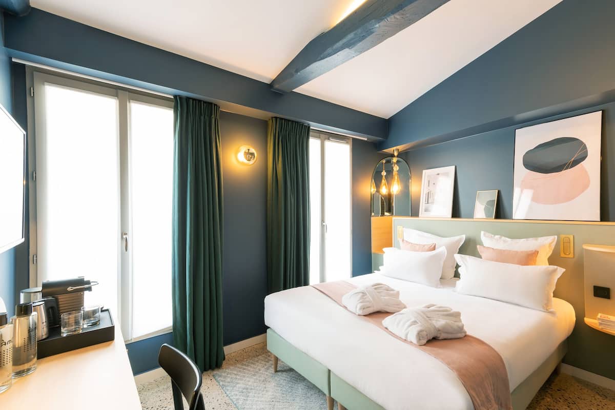 A hotel room with a bed, bedside table, and a large window with curtains.
