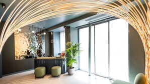 A modern interior with a curved ceiling light, a reception desk, a green cushioned bench, and a potted plant. - Hôtel Amoi Paris (Paris)