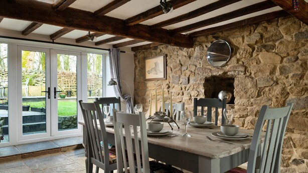 A dining area with a stone wall, wooden beams, and a table set for four.