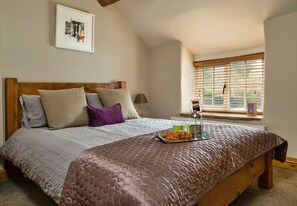 Un dormitorio con una cama de madera, una ventana con persianas, un cuadro enmarcado en la pared y una bandeja con croissants sobre la cama.