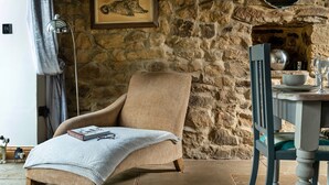 A cozy room with a stone wall, a wooden chair, a table with a bowl and glass, and a book on the chair.