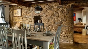A rustic dining area with stone walls, wooden beams, and a stone fireplace.