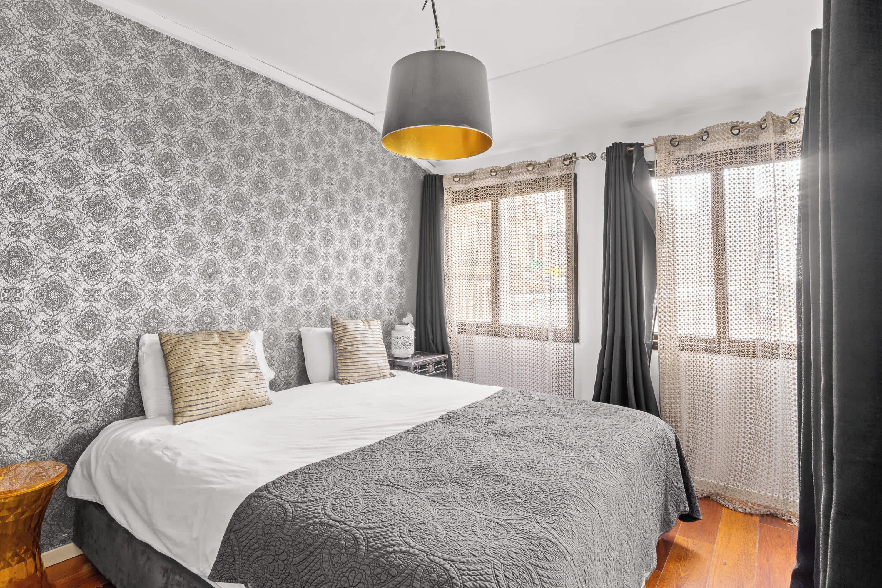 A neatly arranged bedroom with a large bed, patterned wallpaper, and a hanging light fixture.