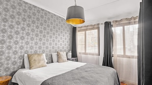 A neatly arranged bedroom with a large bed, patterned wallpaper, and a hanging light fixture.