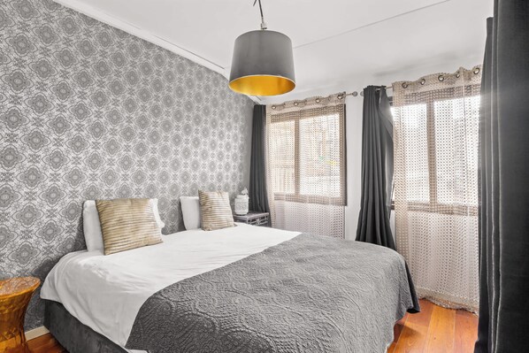 A neatly arranged bedroom with a large bed, patterned wallpaper, and a hanging light fixture.