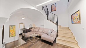 A modern living room with a beige sectional sofa, a glass coffee table, and a staircase with a black railing.