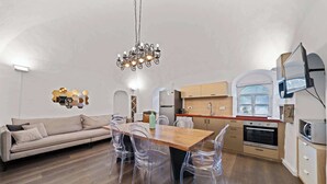 A modern kitchen with a wooden dining table, clear chairs, a chandelier, and built-in appliances.