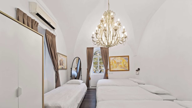 A bedroom with two beds, a chandelier, a window with curtains, and artwork on the walls.