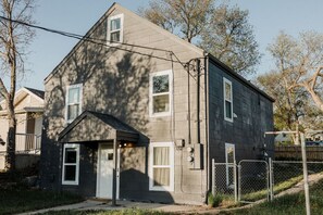A two-story residential building with a grey exterior, a front porch, and a fenced yard. - N 7th Street · Fun Stay in the Heart of Rapid City (Rapid City)