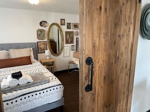 Une chambre à coucher bien rangée, avec un lit, une porte en bois, un miroir et divers tableaux encadrés accrochés au mur.