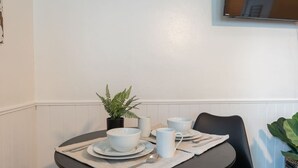 A dining table set with plates, bowls, and utensils, a potted plant, and a television mounted on the wall.