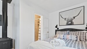 A bedroom with a bed, a black heater, a door leading to a bathroom, and a wall-mounted picture of a bull.