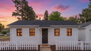 A single-story house with a dark front door, three windows, and a white picket fence.