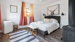A bedroom with a bed, a heater, a window with curtains, a wall-mounted lamp, and a framed picture.