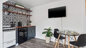 A modern kitchen with a black and white patterned backsplash, a flat-screen TV mounted on the wall, a dining area with a table and chairs, and a built-in oven.