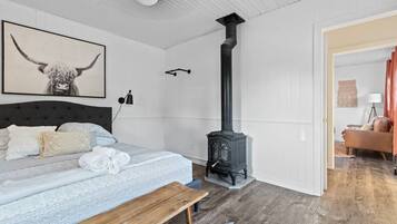 Ein Schlafzimmer mit einem Bett, einer hölzernen Bank, einem schwarzen Herd und einem gerahmten Bild an der Wand.
