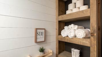A wooden shelf with rolled towels, a small potted plant, and a framed sign with the text 'STAY awhile'.