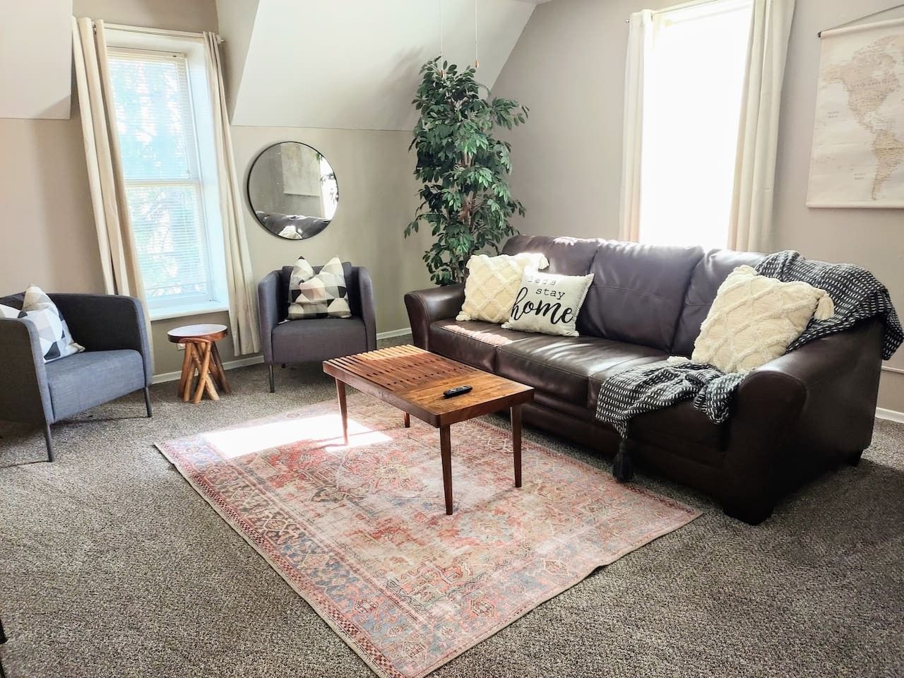 A living room with a brown leather couch, a wooden coffee table, a patterned rug, a small round table, and a potted plant.