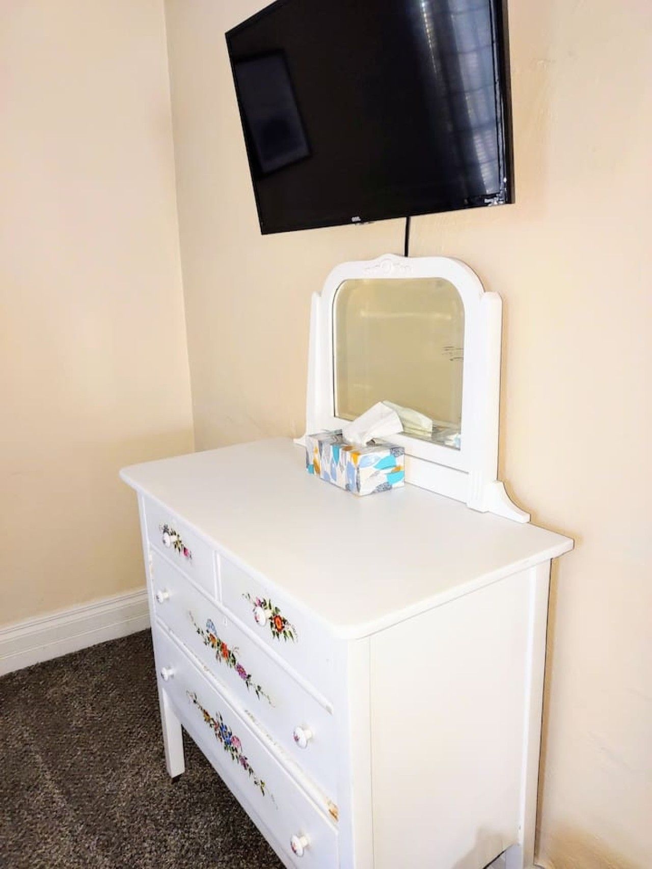A white dresser with floral patterns, a mirror, and a tissue box.