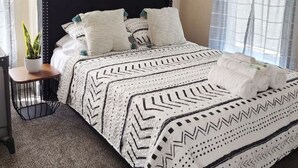 Un dormitorio con una cama, una mesita de noche con una planta y una ventana con cortinas.