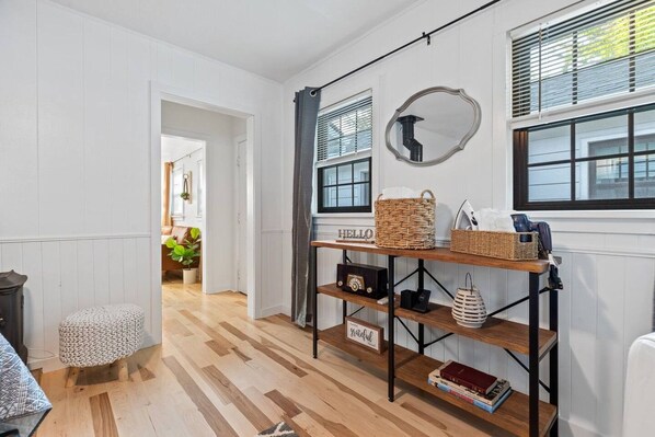 A room with a wooden floor, a white wall, a table with baskets, a radio, and a mirror.