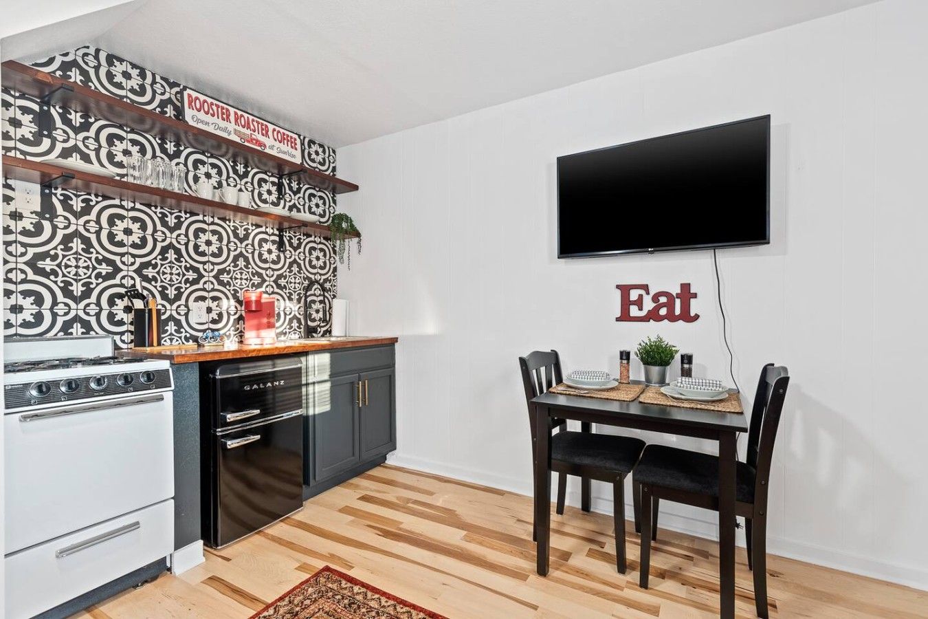 A modern kitchen with a Galanz stove, a flat-screen TV mounted on the wall, and a dining area with a table and chairs.