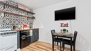 Eine moderne Küche mit einem Galanz-Kochfeld, einem Esstisch mit Stühlen, einem Flachbildfernseher und einem an der Wand befestigten Schild mit der Aufschrift 'Eat'.