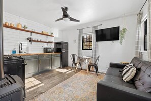 A modern kitchen with a black refrigerator, a microwave, and a stove. There is a dining area with a table and chairs, and a black leather sofa with a patterned pillow. - Cottage#6 - Spearfish Orchard Creek Cottages (Spearfish)